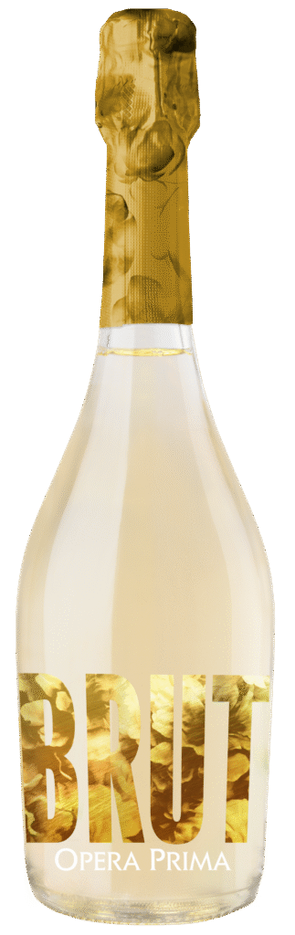 A bottle of Opera Prima Brut sparkling wine with gold foil on the neck and large gold letters spelling BRUT on the label. The bottle contains a pale, light-colored wine.