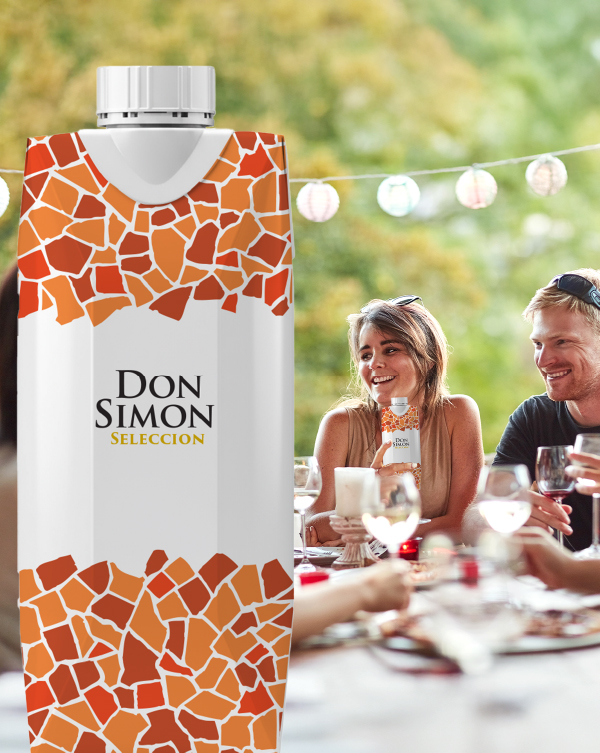 A carton of Don Simon Selección juice is in the foreground, with smiling people enjoying a meal and drinks outdoors in the blurred background, under string lights.